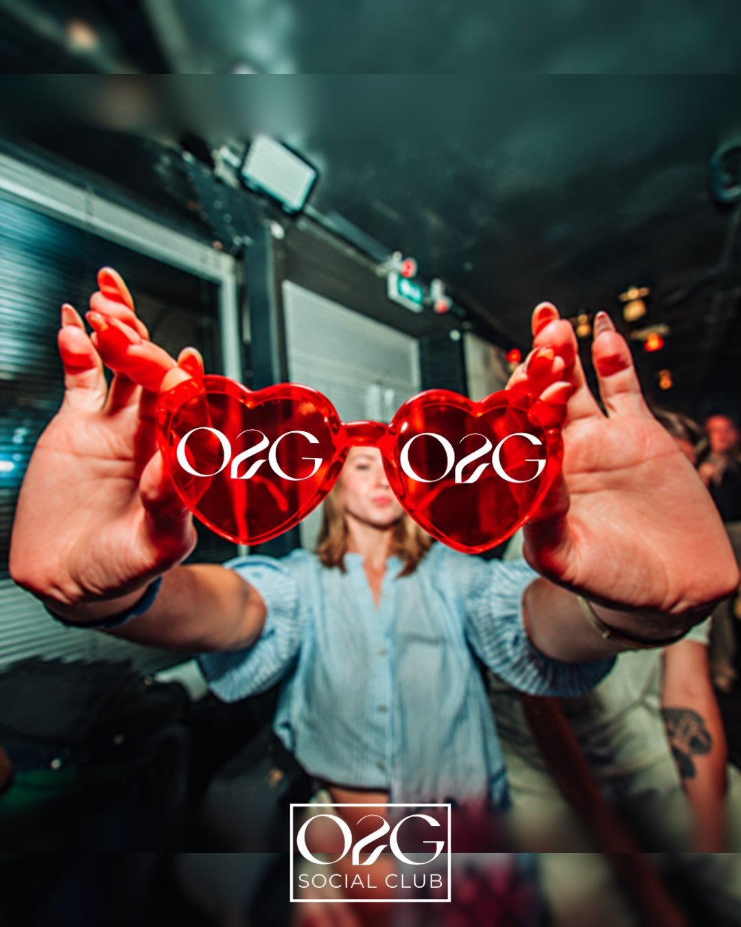Une fêtarde tend des lunettes cœur rouges marquées O2G vers l’objectif